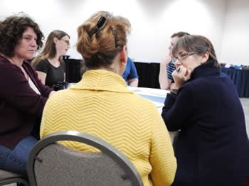 People sitting around a table the woman in the middle has her back turned and is wearing a yellow jacket