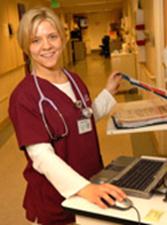 A blonde woman in scrubs smiles at the camera