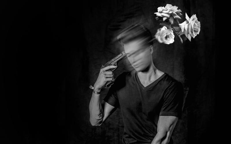 black and white photo of a young man with a gun to his head with flowers on the other side of his head.