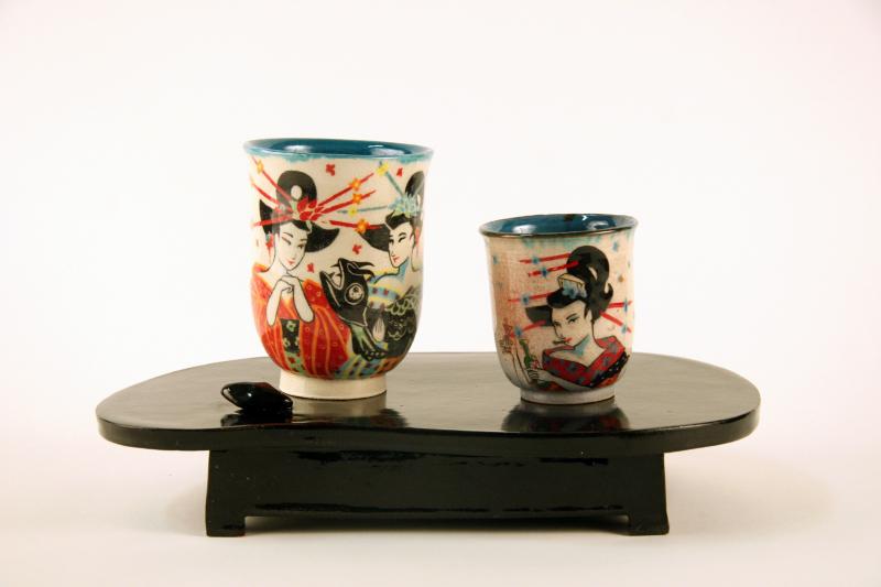 Ceramic tea and sake cups with images of Japanese women on a wooden stand