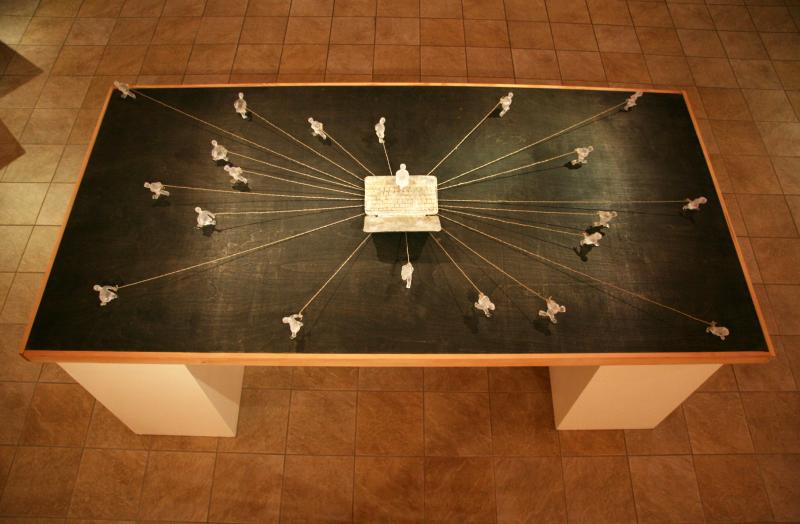 small carved figurines on a large wood table attached by string to a carved figurine in the middle