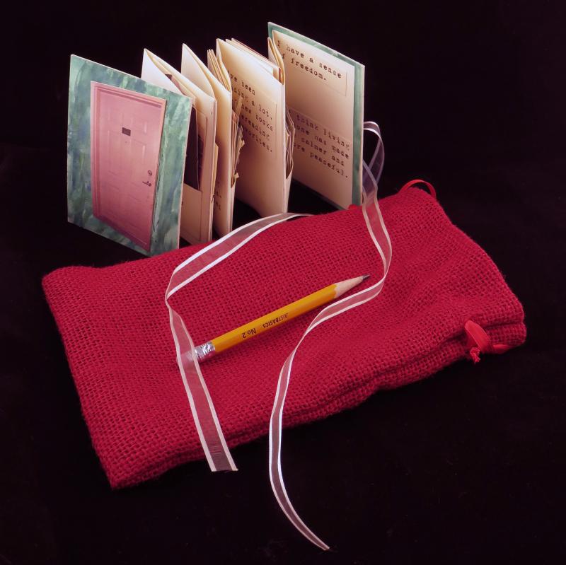 picture of an accordian shaped bound book near a pink bag it is kept in with a pencil on the bag