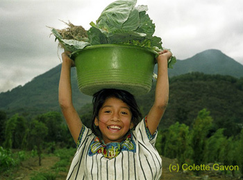 smiling girl holding basket of vegetables on her head
